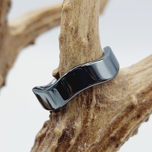 May include: A black hematite ring with a wavy design. The ring is on a piece of antler.