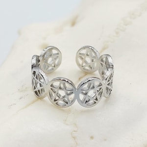May include: A silver adjustable ring featuring a repeating pattern of five-pointed stars. The ring is made of metal and has a polished finish.