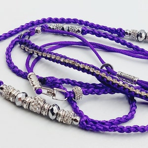 May include: A purple braided cord with silver beads and a silver clasp. The cord is decorated with rhinestones.