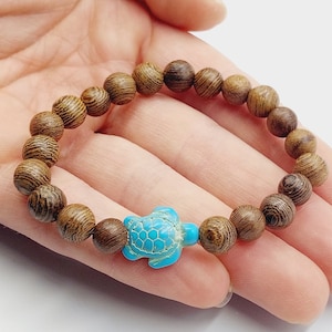 Op de afbeelding: Een bruine houten kralen armband met een turquoise schildpad bedel.