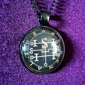 May include: A black necklace with a round pendant featuring a silver sigil on a black background. The pendant has the words "SATOR AREPO TENET OPERA ROTAS" inscribed around the edge.