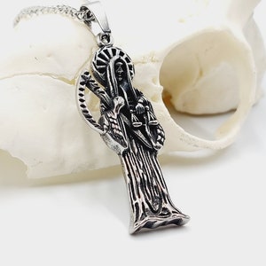 Può includere: Una collana con un ciondolo d'argento che presenta una rappresentazione dettagliata di Santa Muerte, la santa patrona della morte nella religione popolare messicana. Il ciondolo è appeso a una catena d'argento.