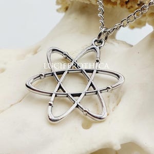 May include: A silver-toned metal pendant shaped like an atom with intersecting elliptical orbits, suspended from a matching silver-toned chain. The pendant features the text LUCIFEROTHICA engraved across the center of the atomic structure.