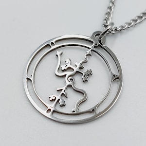 May include: A silver necklace with a circular pendant featuring a stylised tree design. The pendant is made of metal and has a delicate, intricate design.