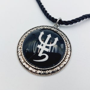 May include: A silver pendant necklace with a black circular charm featuring a white trident symbol. The necklace has a black cord.