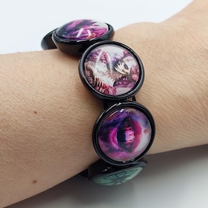 May include: Black elastic bracelet with colorful round charms featuring images of a skull, lips, and flowers.