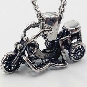 May include: A silver-toned pendant in the shape of a three-wheeled motorcycle. The pendant has a detailed design and is attached to a silver chain.