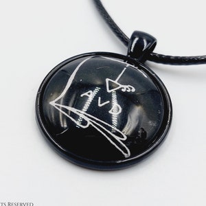 May include: A black necklace with a round pendant featuring a white sigil design. The pendant is made of glass and has a black metal frame.