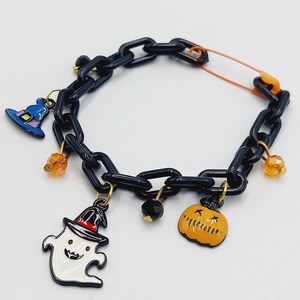 May include: A black chain bracelet with Halloween-themed charms, including a ghost, a pumpkin, a witch's hat, and orange beads.