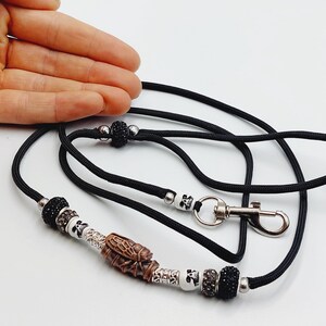 Puede incluir: Cordón de paracord negro con un cierre plateado y un dije de cuentas que incluye una calavera, una cuenta de madera marrón y cuentas negras y plateadas.
