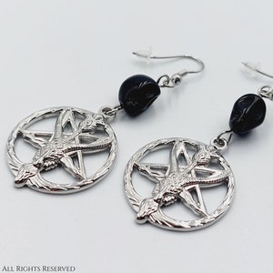 Op de afbeelding: Zilveren oorbellen met een pentagram en geitenkopontwerp, elke oorbel heeft een zwarte schedelkraal.