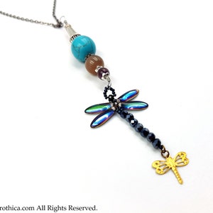 May include: A silver chain necklace with turquoise, brown, and purple beads. An iridescent dragonfly charm hangs from the beads, with a gold dragonfly charm at the bottom.