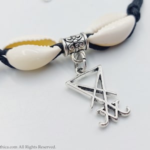 May include: A black cord bracelet with two white seashells and a silver charm featuring a pentagram symbol.