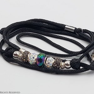 May include: Black braided cord leash with a silver clasp and a beaded charm. The charm features a large iridescent bead surrounded by smaller silver and crystal beads.
