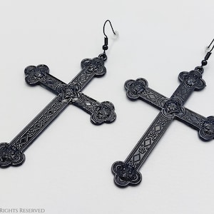 May include: A pair of black metal earrings featuring ornate cross designs. The crosses have intricate details and a slightly aged finish.