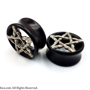 May include: A pair of black wood ear gauges with a silver pentagram design. The pentagram is made of twisted metal that resembles branches.