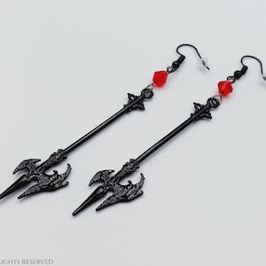 May include: A pair of black arrow earrings with red crystal accents. The arrowheads are detailed with a gothic design.