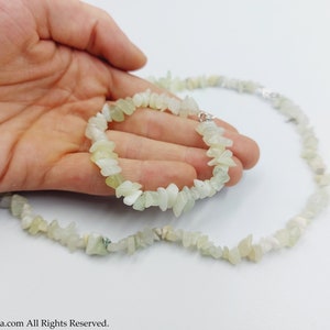 Op de afbeelding: Een set van twee kettingen gemaakt van lichtgroene jade-chips. De kettingen liggen op een hand, met de kortere ketting om de pols en de langere ketting om de nek.
