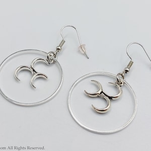 May include: Silver hoop earrings with a triple crescent moon charm hanging from each hoop.