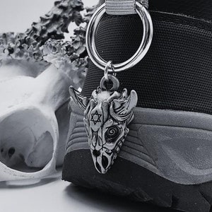 May include: A black high-top shoe with a silver charm attached to the laces. The charm is a detailed skull with a star and a circle design.