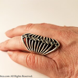 Pu&ograve; includere: Un anello d'argento con un design a forma di ventaglio e pietre preziose blu. L'anello &egrave; indossato su un dito.