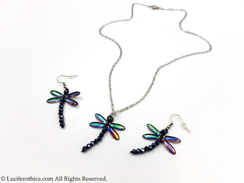 May include: A silver chain necklace and a pair of earrings featuring iridescent dragonfly pendants with black bead accents.
