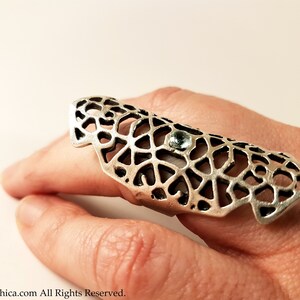 May include: A silver ring with a delicate, intricate design and a small, clear gemstone. The ring is worn on a finger and is a statement piece.