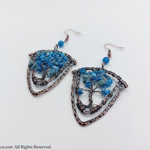 May include: A pair of copper wire earrings with a tree of life design. The tree is made of blue and green gemstone chips. The earrings are in the shape of a triangle.