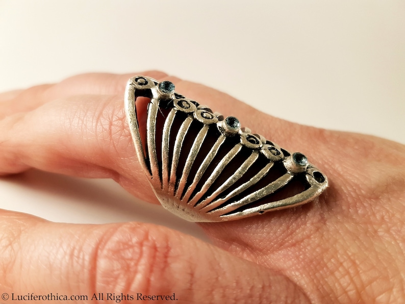 Pu&ograve; includere: Un anello d'argento con un design a forma di ventaglio e pietre preziose blu. L'anello &egrave; indossato su un dito.