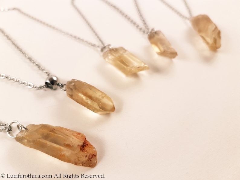 May include: Five silver necklaces with yellow crystal pendants. The crystals are all different sizes and shapes.