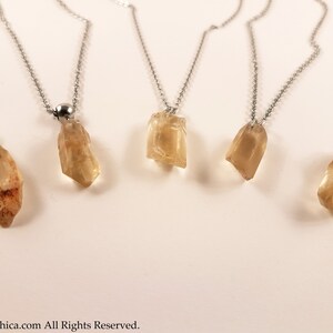 May include: Five silver necklaces with raw, light brown, crystal pendants. The necklaces are on a white background.
