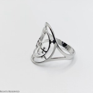 May include: A silver ring with a geometric design featuring an anchor symbol. The ring is open and has a wide band.