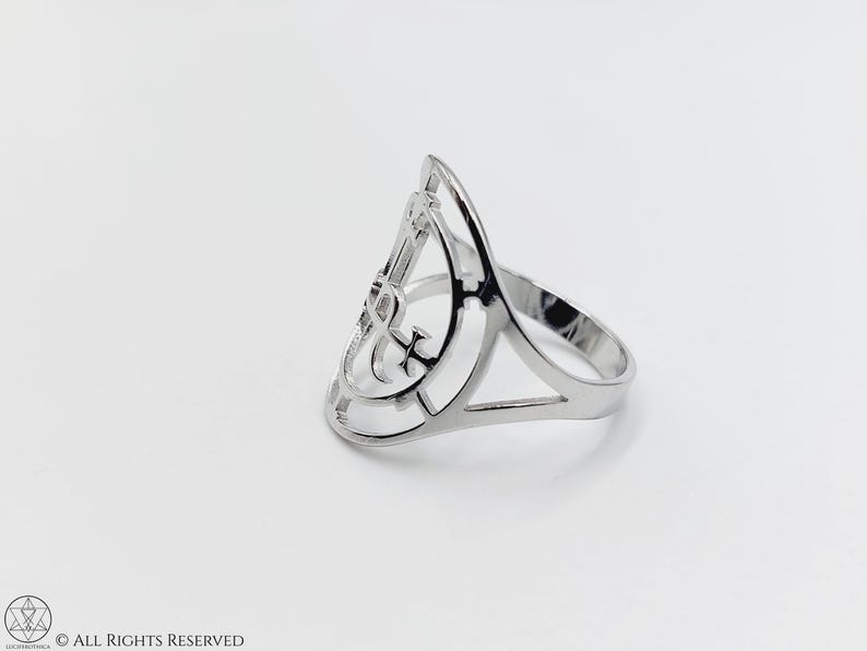 May include: A silver ring with a geometric design featuring an anchor symbol. The ring is open and has a wide band.