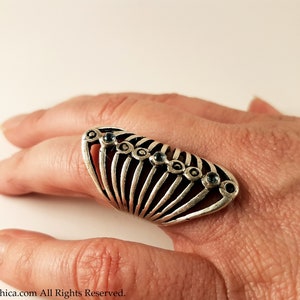 Pu&ograve; includere: Un anello d'argento con un design geometrico e pietre preziose blu. L'anello &egrave; indossato su un dito.