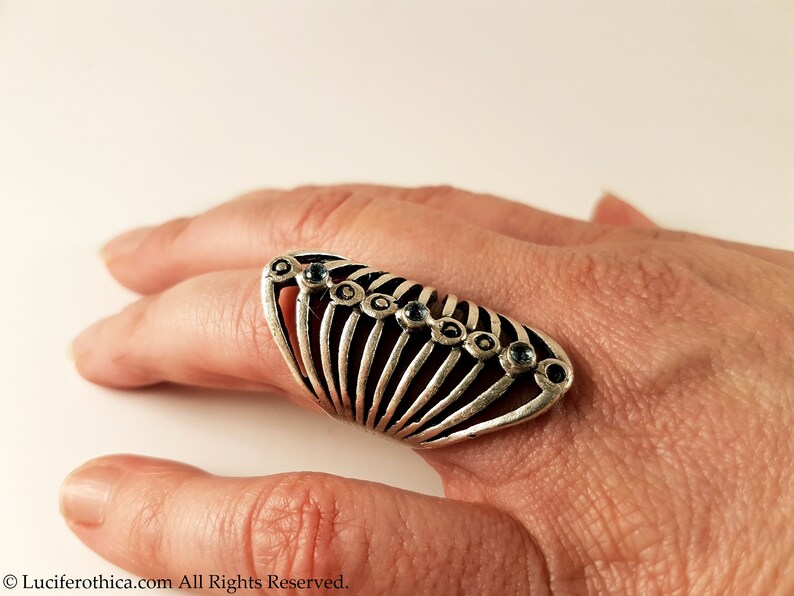 Pu&ograve; includere: Un anello d'argento con un design geometrico e pietre preziose blu. L'anello &egrave; indossato su un dito.