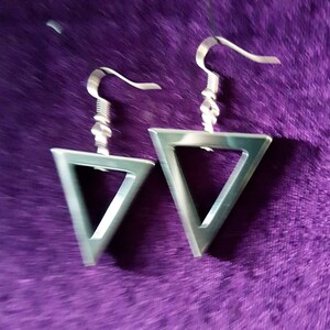 May include: A pair of silver triangle earrings with a simple design. The earrings are hanging from a purple velvet surface.
