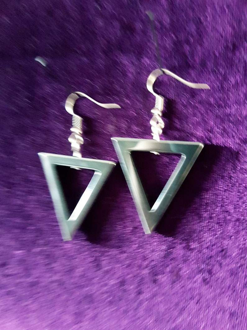 May include: A pair of silver triangle earrings with a simple design. The earrings are hanging from a purple velvet surface.