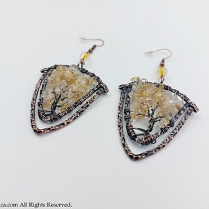 May include: A pair of copper wire earrings featuring a tree design and clear quartz crystals. The earrings are shaped like a triangle and have a hammered finish.