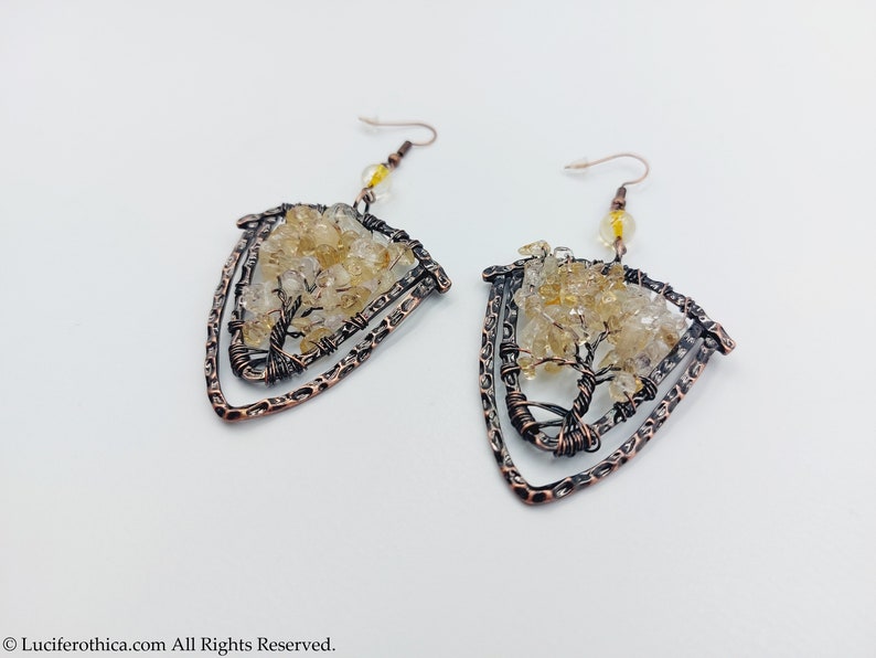 May include: A pair of copper wire earrings featuring a tree design and clear quartz crystals. The earrings are shaped like a triangle and have a hammered finish.