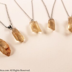 May include: Five silver necklaces with different sized, clear, light brown crystal pendants. The necklaces are on a white background.