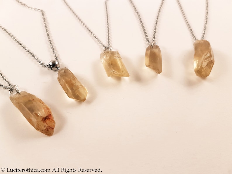 May include: Five silver necklaces with different sized, clear, light brown crystal pendants. The necklaces are on a white background.