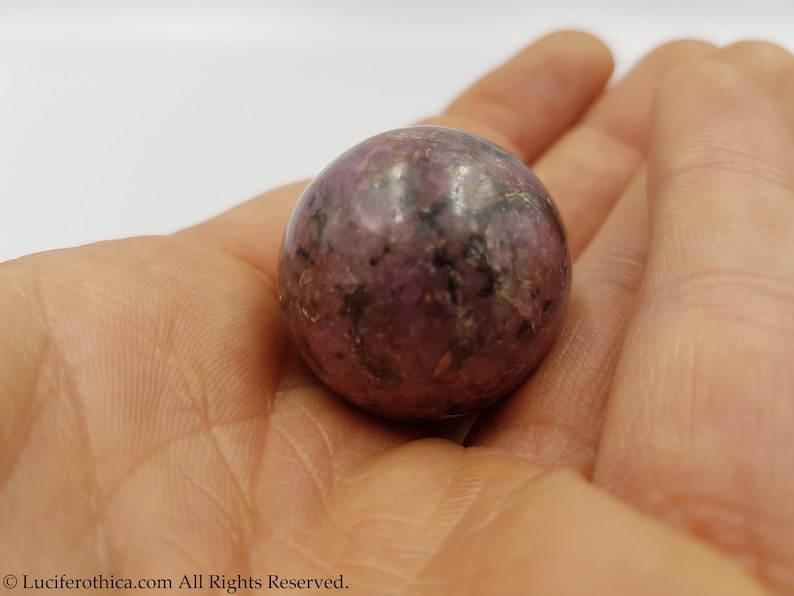 May include: A smooth, round, purple and black gemstone sphere.