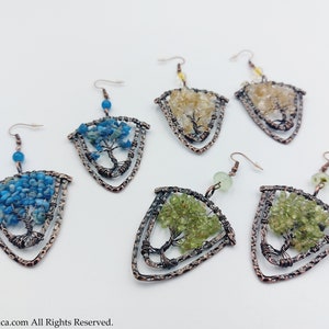 May include: A set of six earrings featuring a tree of life design with different coloured gemstones. The earrings are made of copper wire and feature a triangular shape. The gemstones are blue, green, and yellow.