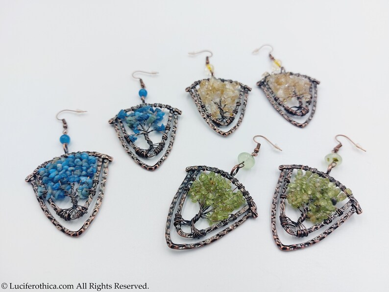 May include: A set of six earrings featuring a tree of life design with different coloured gemstones. The earrings are made of copper wire and feature a triangular shape. The gemstones are blue, green, and yellow.