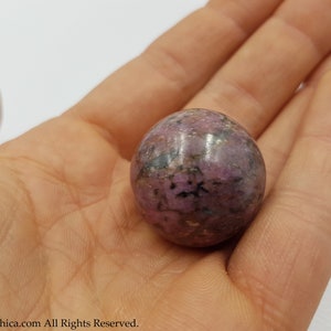 May include: A smooth, polished purple and black sphere of rhodonite, a crystal known for its grounding and calming properties.