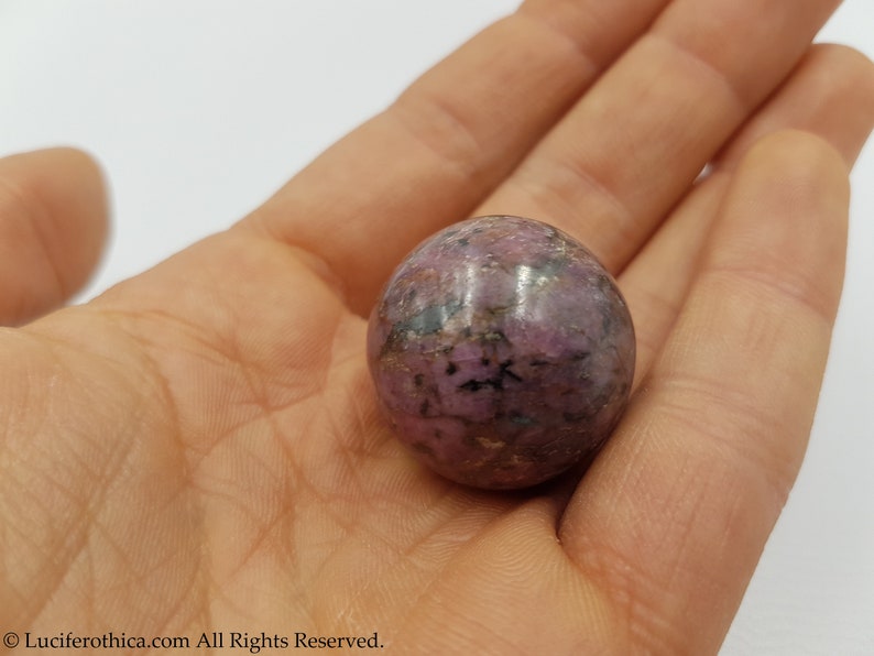 May include: A smooth, polished purple and black sphere of rhodonite, a crystal known for its grounding and calming properties.
