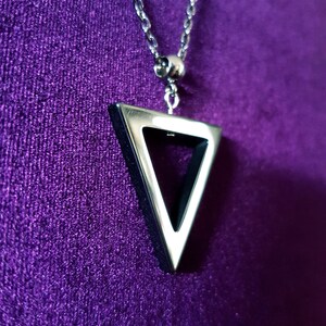 May include: A silver chain necklace with a triangular pendant. The pendant is hollow and has a silver outline.
