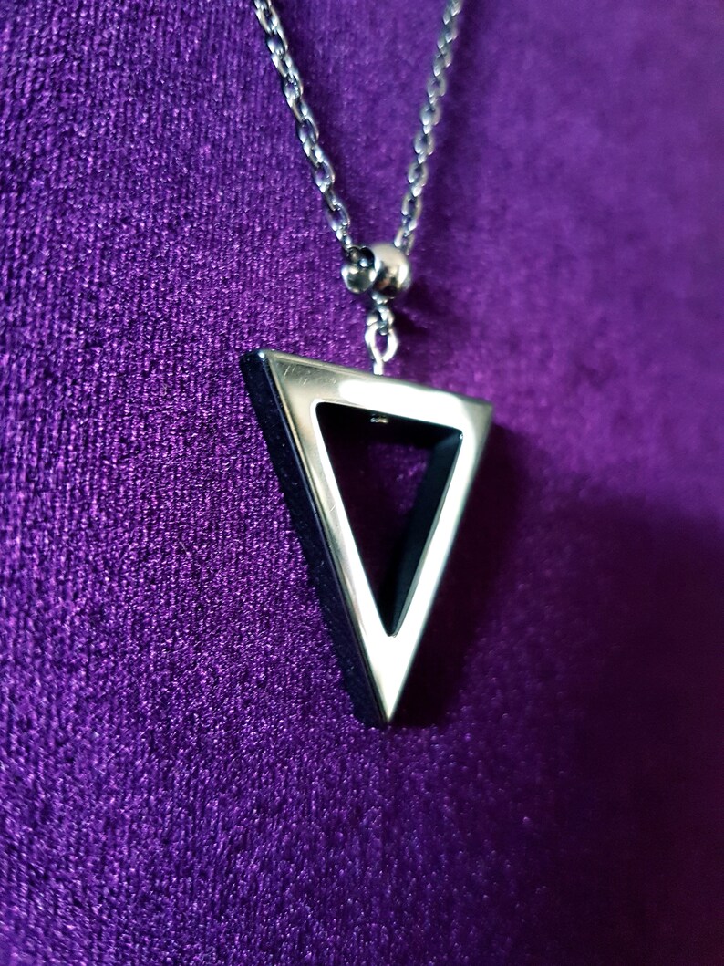 May include: A silver chain necklace with a triangular pendant. The pendant is hollow and has a silver outline.