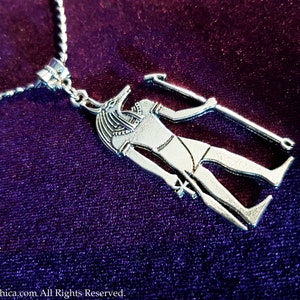 May include: Silver necklace featuring a pendant depicting an Egyptian god with a jackal head, holding a staff. The pendant is detailed and intricate.