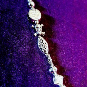 May include: A silver necklace with a skull charm, a decorative bead, and a snake charm. The necklace is on a purple background.